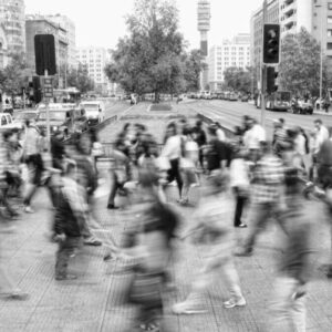 Grayscale photo from “Media Maze” by Annika Brelsford, showing a blurred group of people crossing a city intersection.
