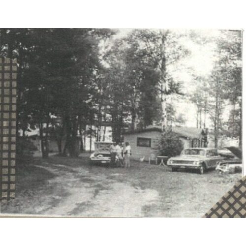 A vintage black and white scrapbook photo of individuals in front of a car with the hood popped open.